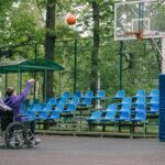 Osoba na wózku gra w koszykówkę z przyjacielem na zewnętrznym boisku