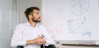 Nowy Polski Ład a prawa osób niepełnosprawnych – co realnie się zmieniło Mężczyzna na wózku inwalidzkim analizuje wykresy na tablicy w biurze